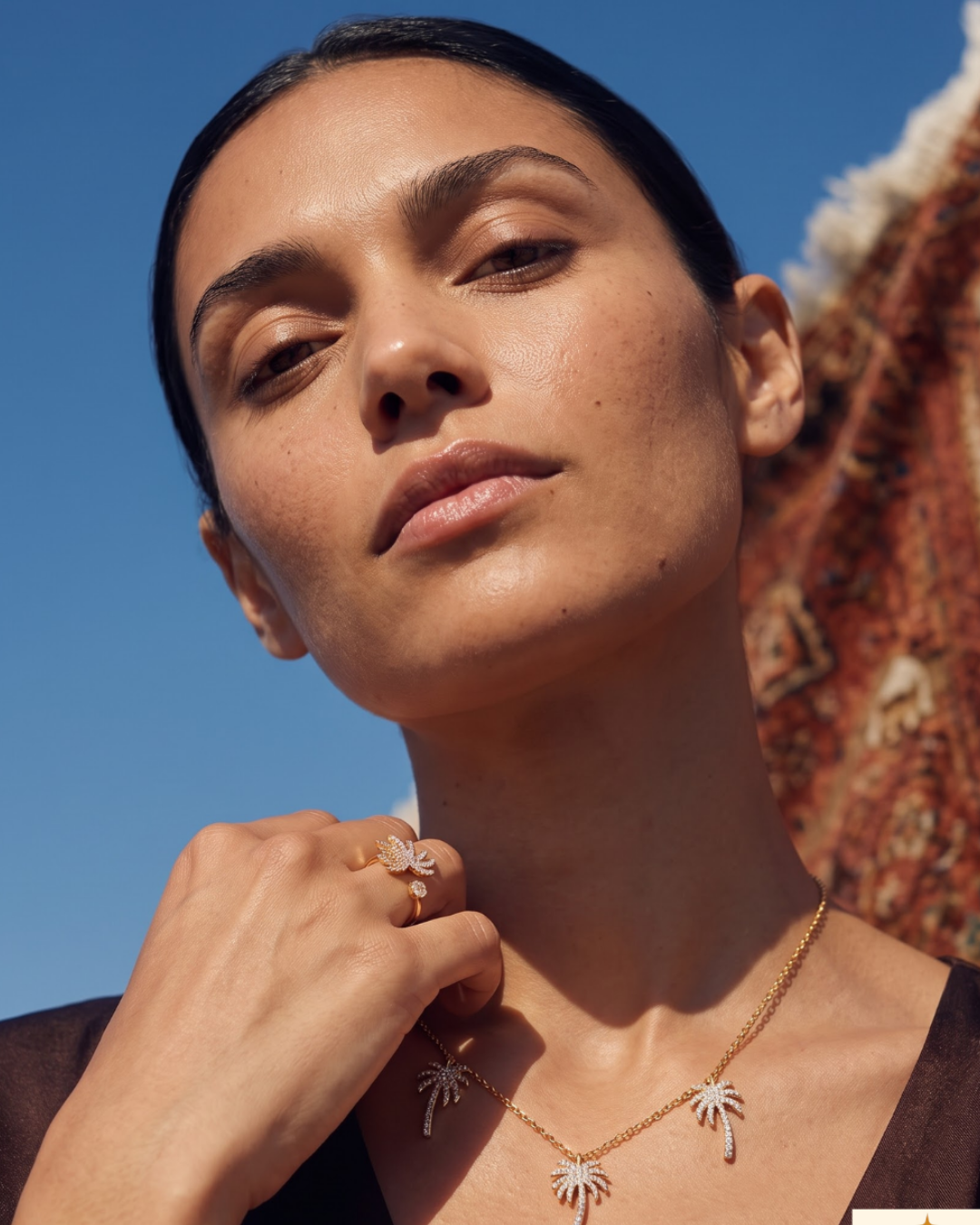 Close portrait against a blue sky of a woman wearing a palm-motif diamond necklace and matching ring
